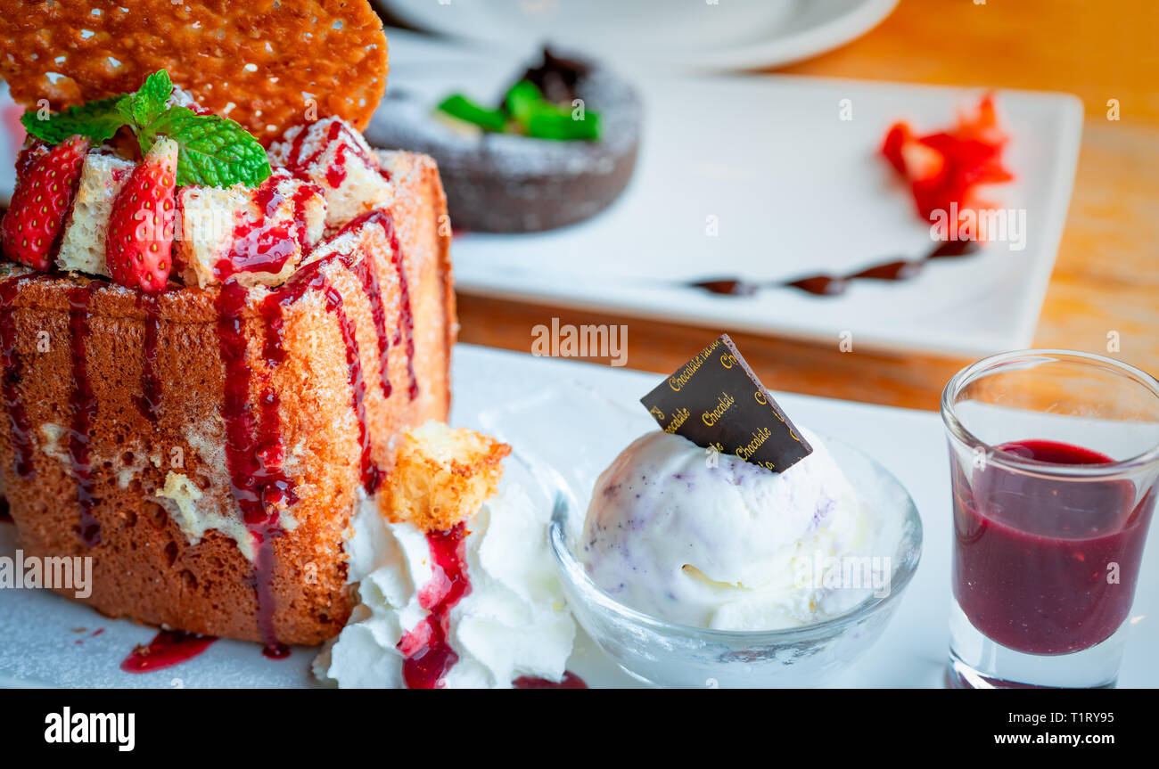 Honey toast topping with strawberries, a side of whipped cream, vanilla ice cream. Bread toast on white dish on blurred background of chocolate lava c Stock Photo