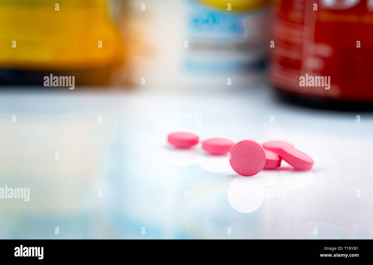 Round pink tablets pill on blurred background of drug bottle