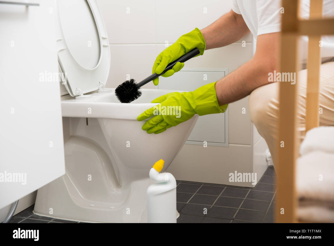 Man in rubber protective gloves cleaning, washing toilet with brush and