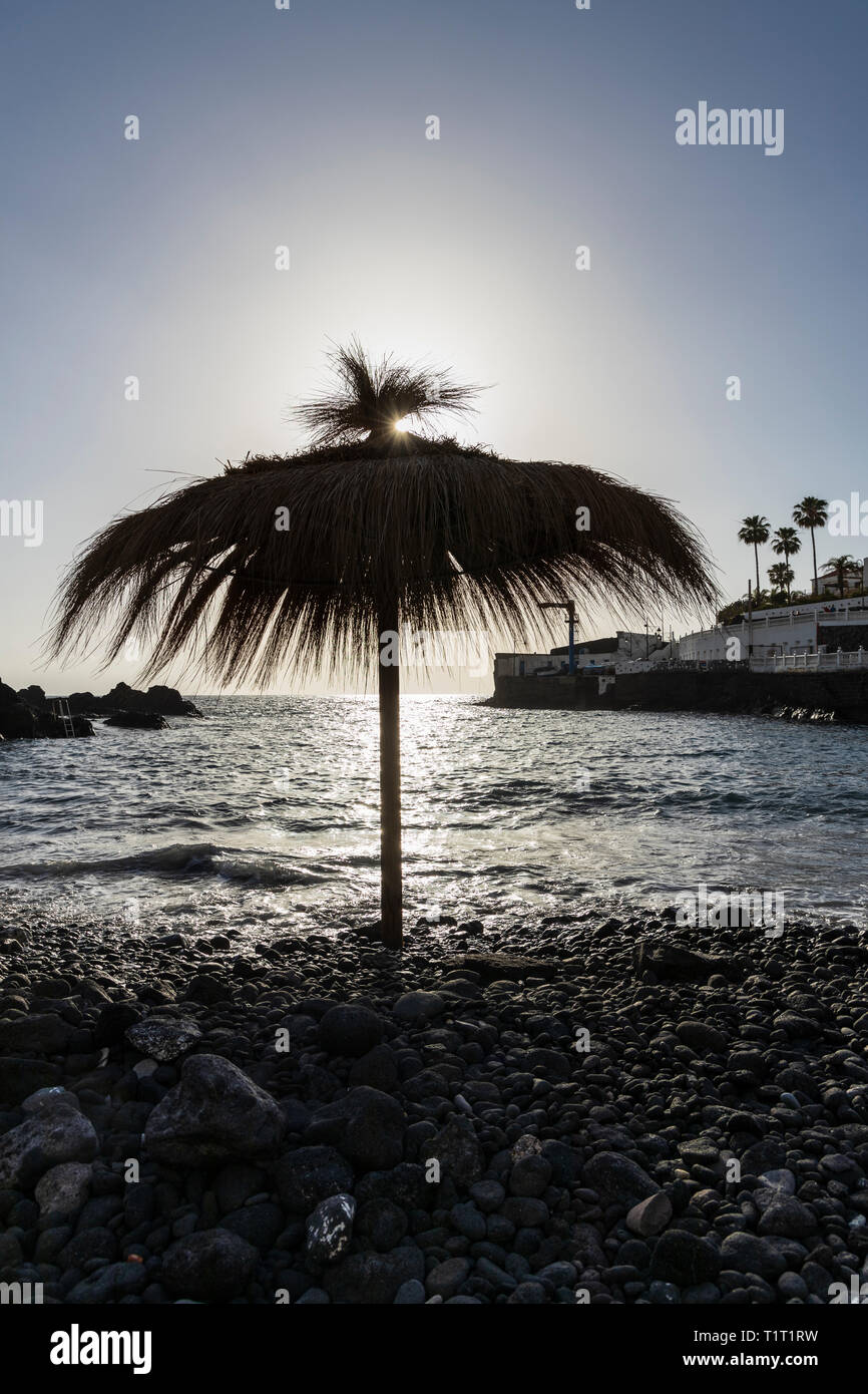 Straw sun umbrella, sunshade, on the stony beach of Playa Chica, Puerto de Santiago, Tenerife, Canary Islands, Spain Stock Photo