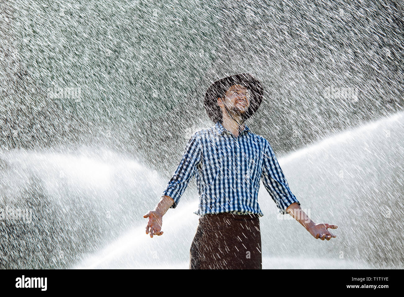 The farmer in the hat is enjoying the rain. Young man getting wet under
