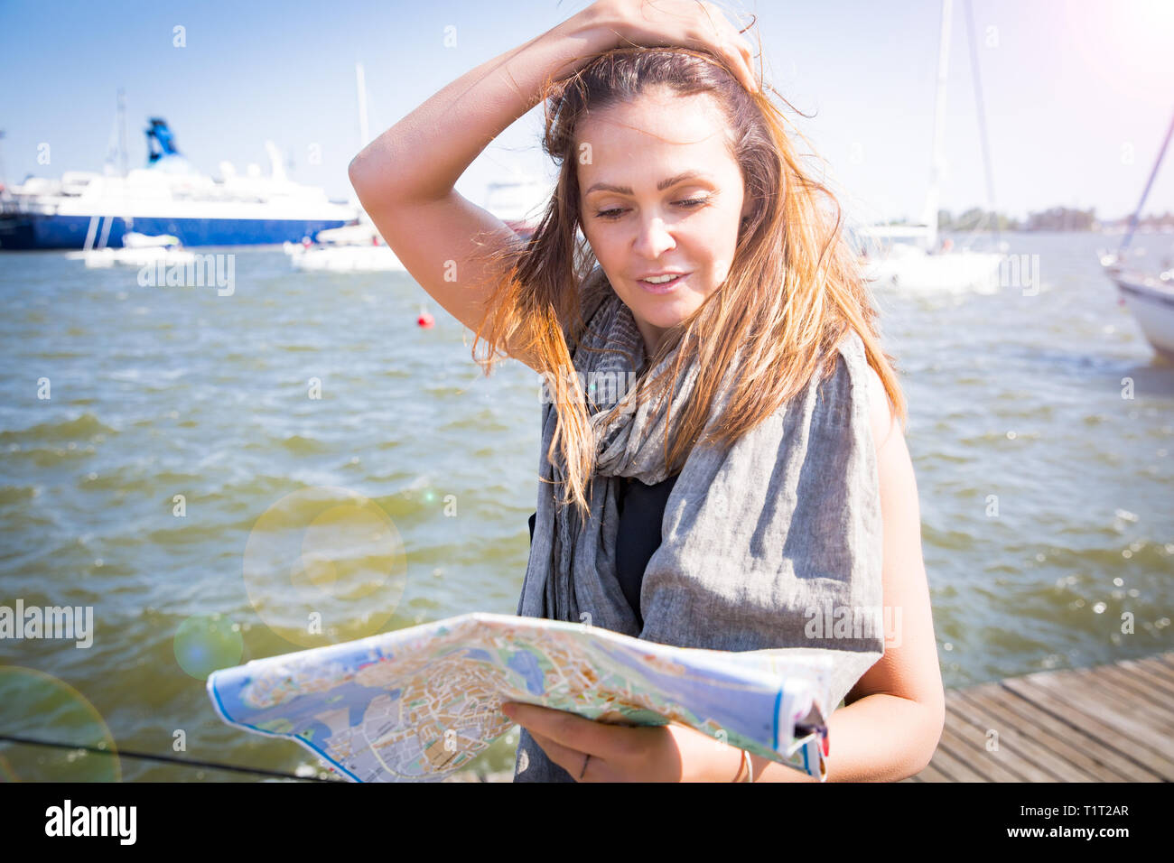 Middle aged woman reading city map, happy tourist pointing into city guide. Search locations, walk along the waterfront, seaside. Sunny summer harbour Stock Photo
