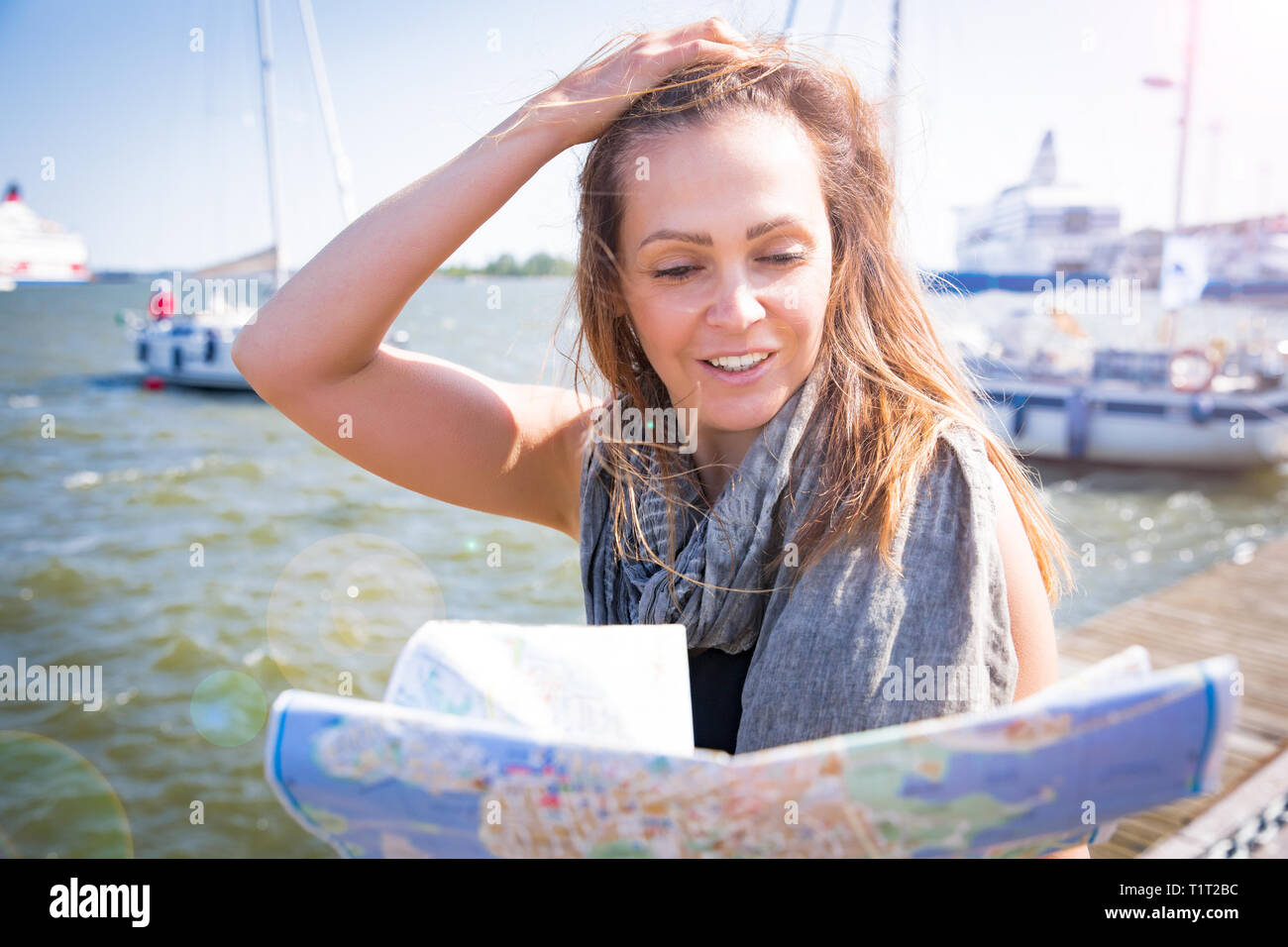 Middle aged woman reading city map, happy tourist pointing into city guide. Search locations, walk along the waterfront, seaside. Sunny summer harbour Stock Photo