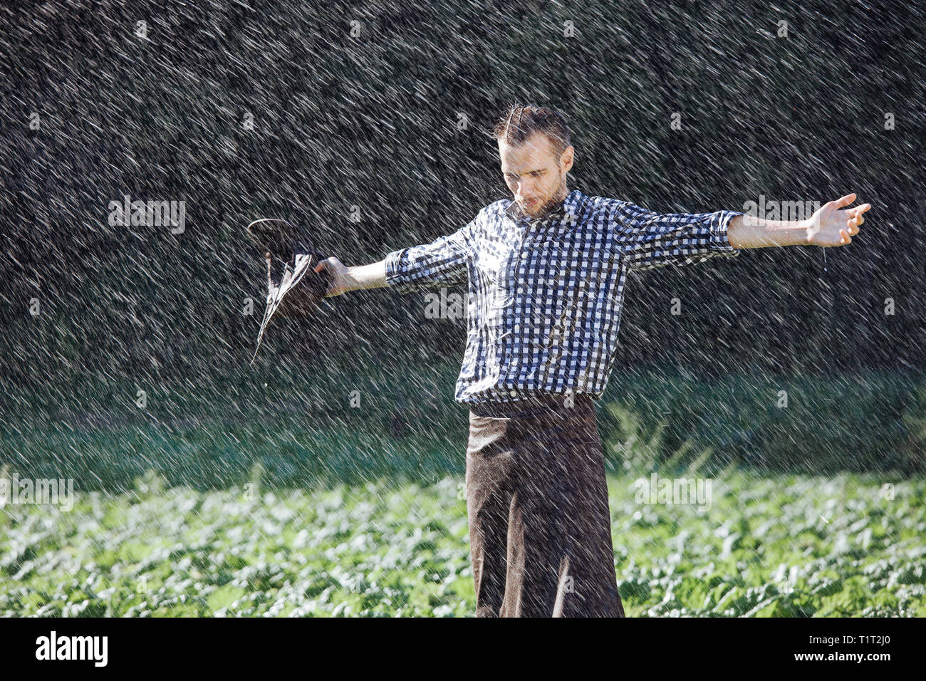 The farmer in the hat is enjoying the rain. Young man getting wet under