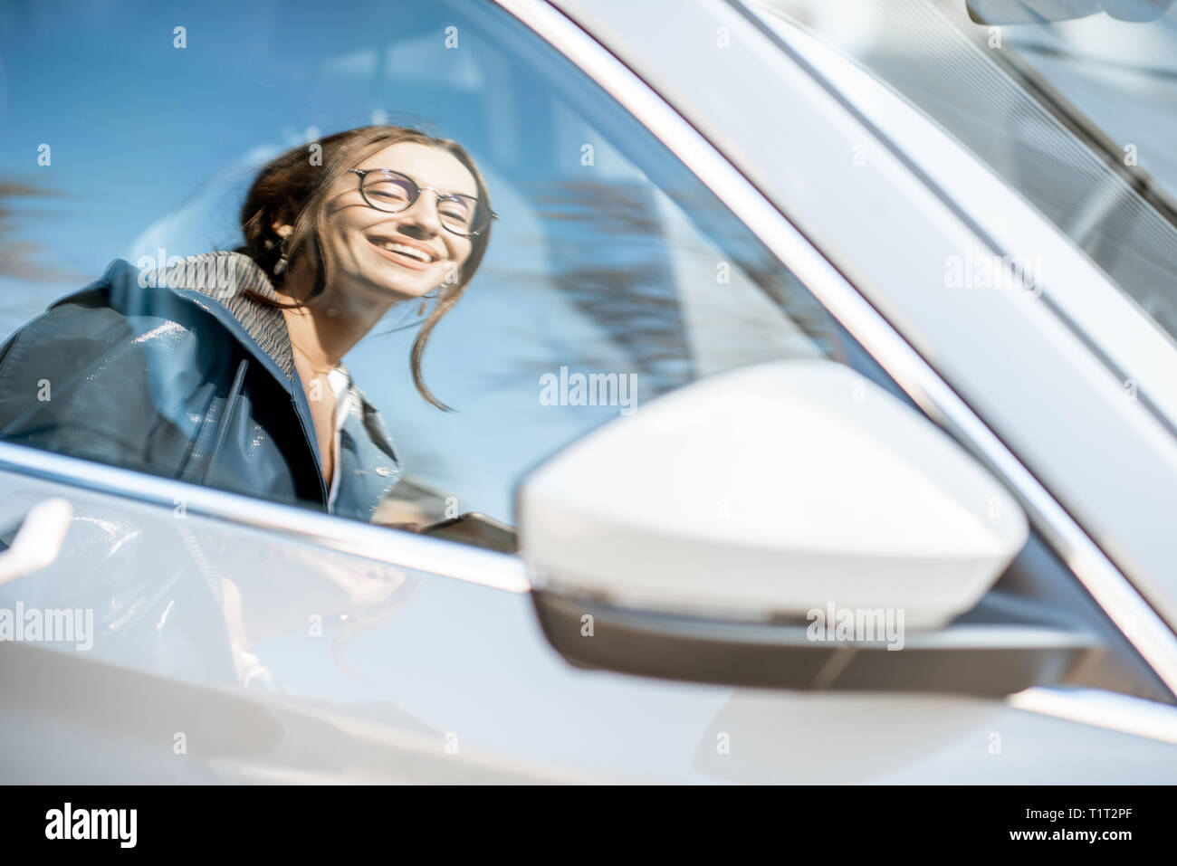 Reflection on the car window of a young stylish woman standing near the ...