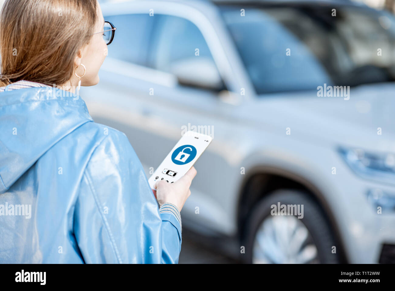 Woman unlocking car using mobile application on a smart phone. Concept of a remote control and car protection through the internet Stock Photo