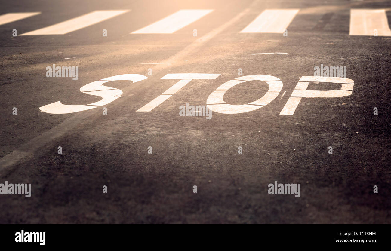 A stop sign painted on the road with crosswalk in the distance Stock Photo