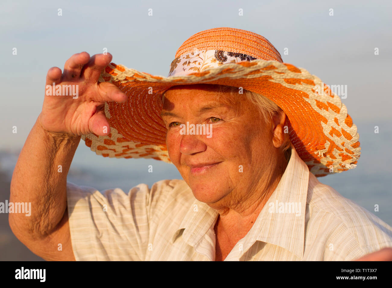 Beautiful elderly woman in a hat on the background of the sea. Face of an old woman with a smile. Grandma on vacation Stock Photo