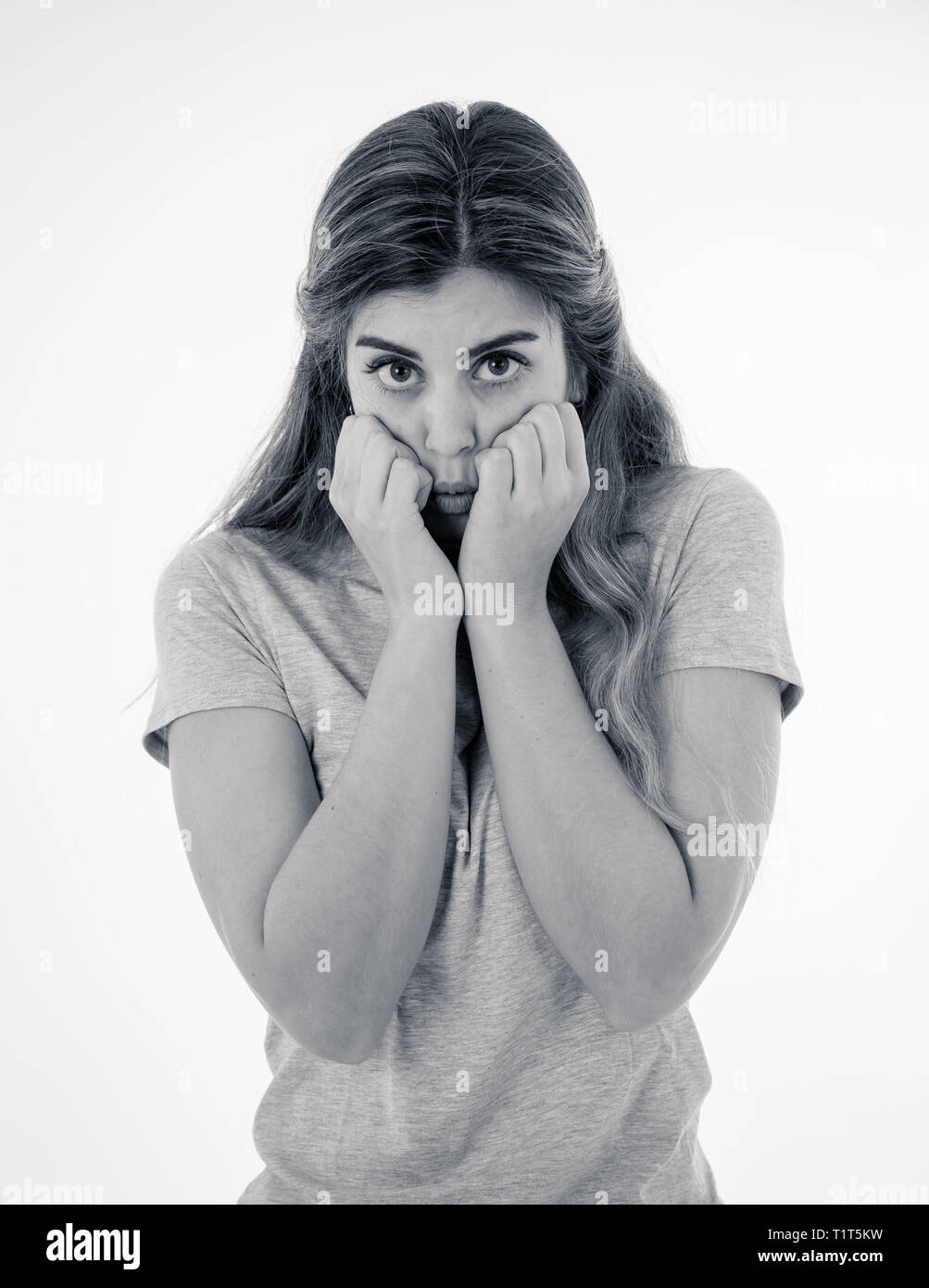 Close up in black and white of young woman feeling afraid and shocked hiding her face from something scary. Looking with fear in her eyes. People and  Stock Photo
