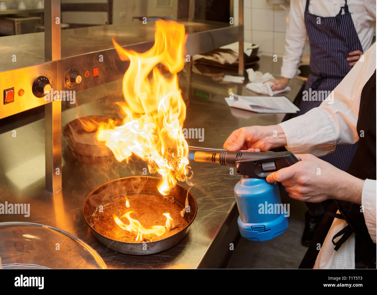 Chef is burning aromatic herbs to smoke a dish, commercial kitchen ...