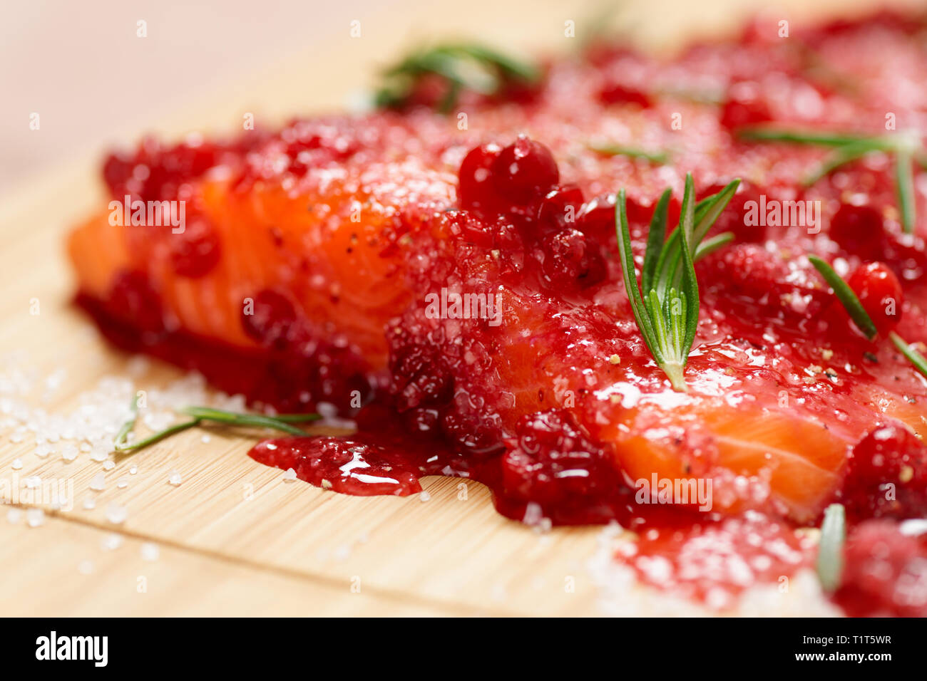 Salmon steak being marinated in salt with rosemary and redberries Stock