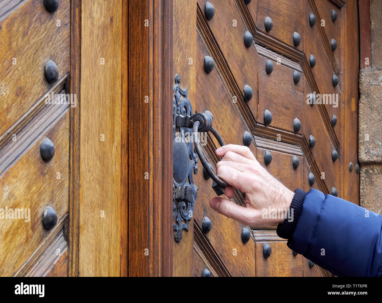 Man holds hand door handle or knocker of old wooden door. It opens the