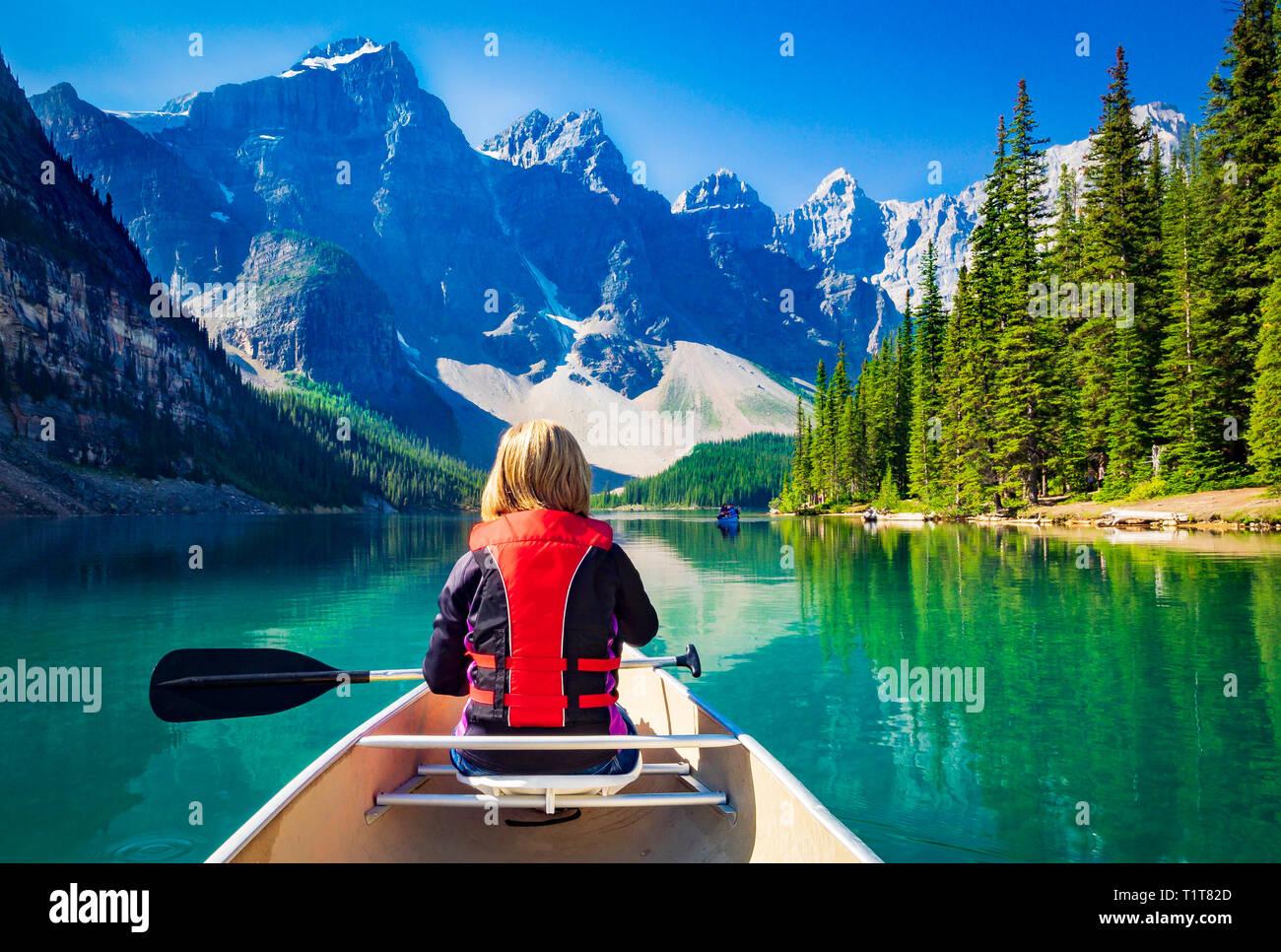 Woman boating in a canoe on Moraine Lake, Canada with mountains in ...