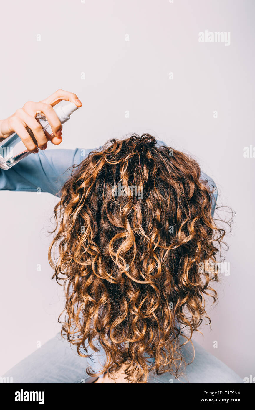 Head of young woman with long curly hair is lowered down to apply cosmetic  care product. Female using spray with sea salt to make beachy waves hairsty  Stock Photo - Alamy