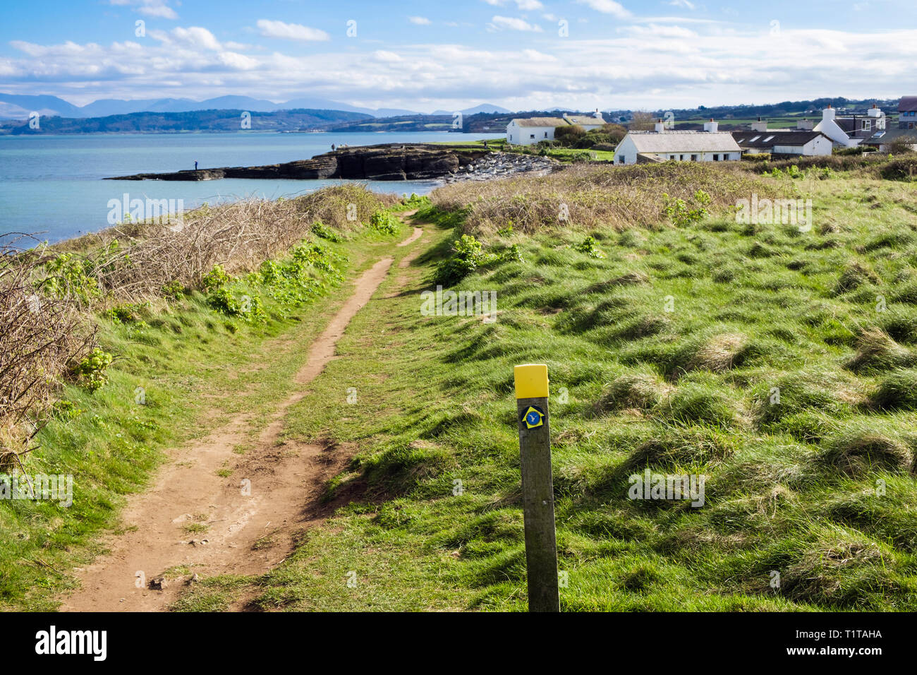Anglesey coastal path and way marker post on Welsh coast with view to distant mountains. Moelfre, Isle of Anglesey, Wales, UK, Britain Stock Photo