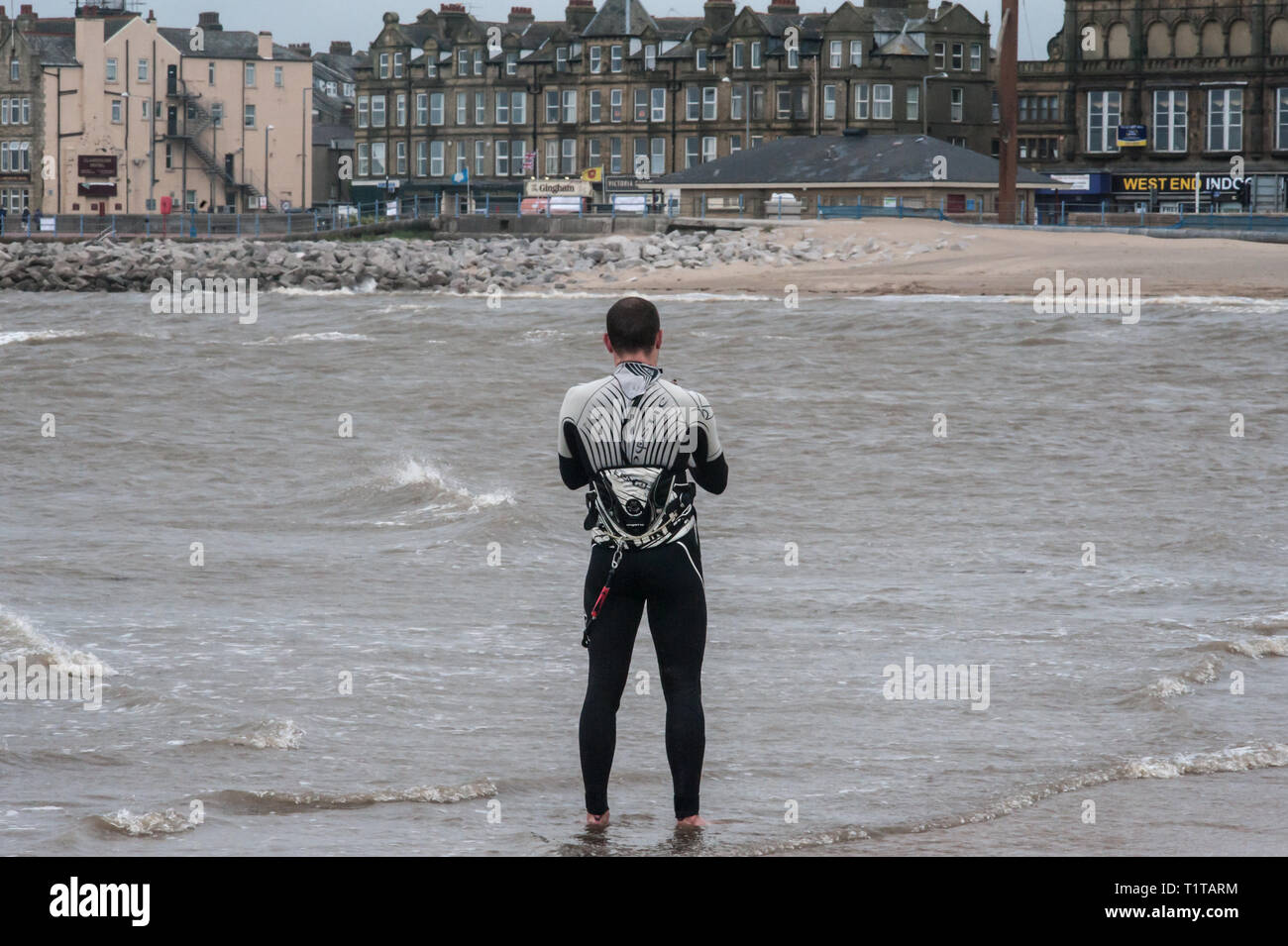 A kite surfer stands in the shallow water on the shore of Morecambe's West End. Stock Photo