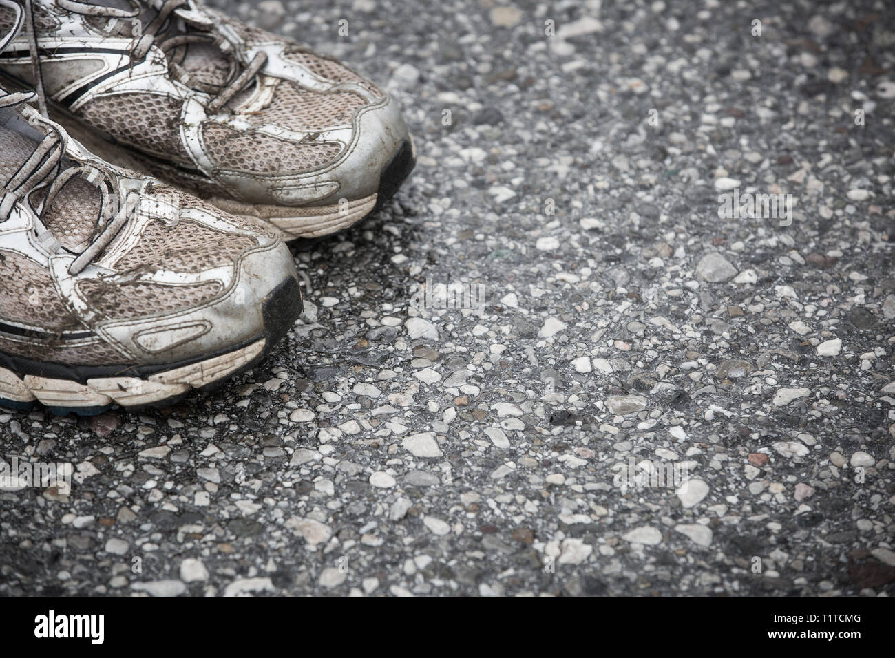 Worn, dirty, smelly and old running shoes on a tarmac road. Road