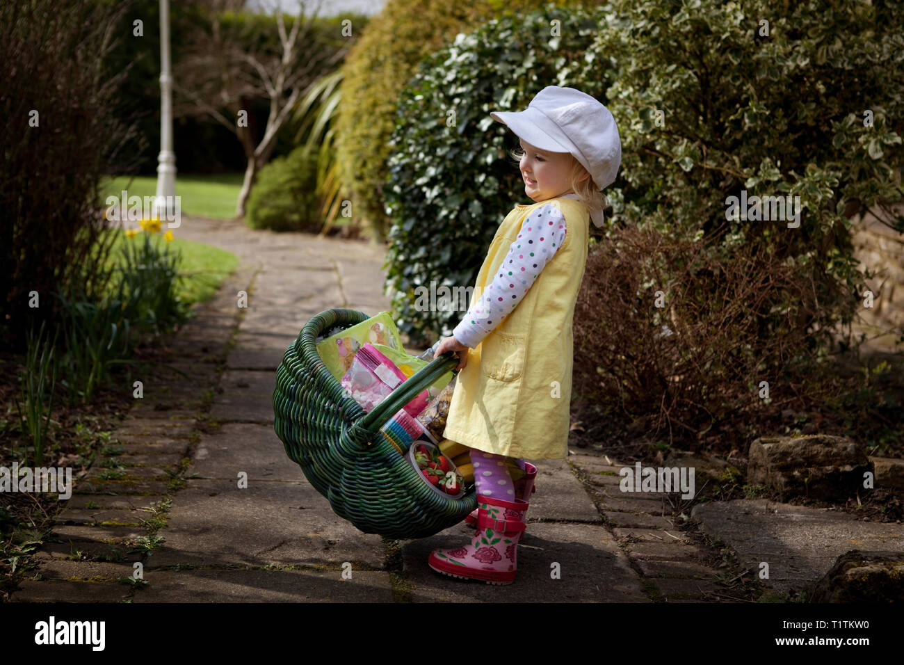 Toddler carrying a green wicker basket full of groceries Stock Photo