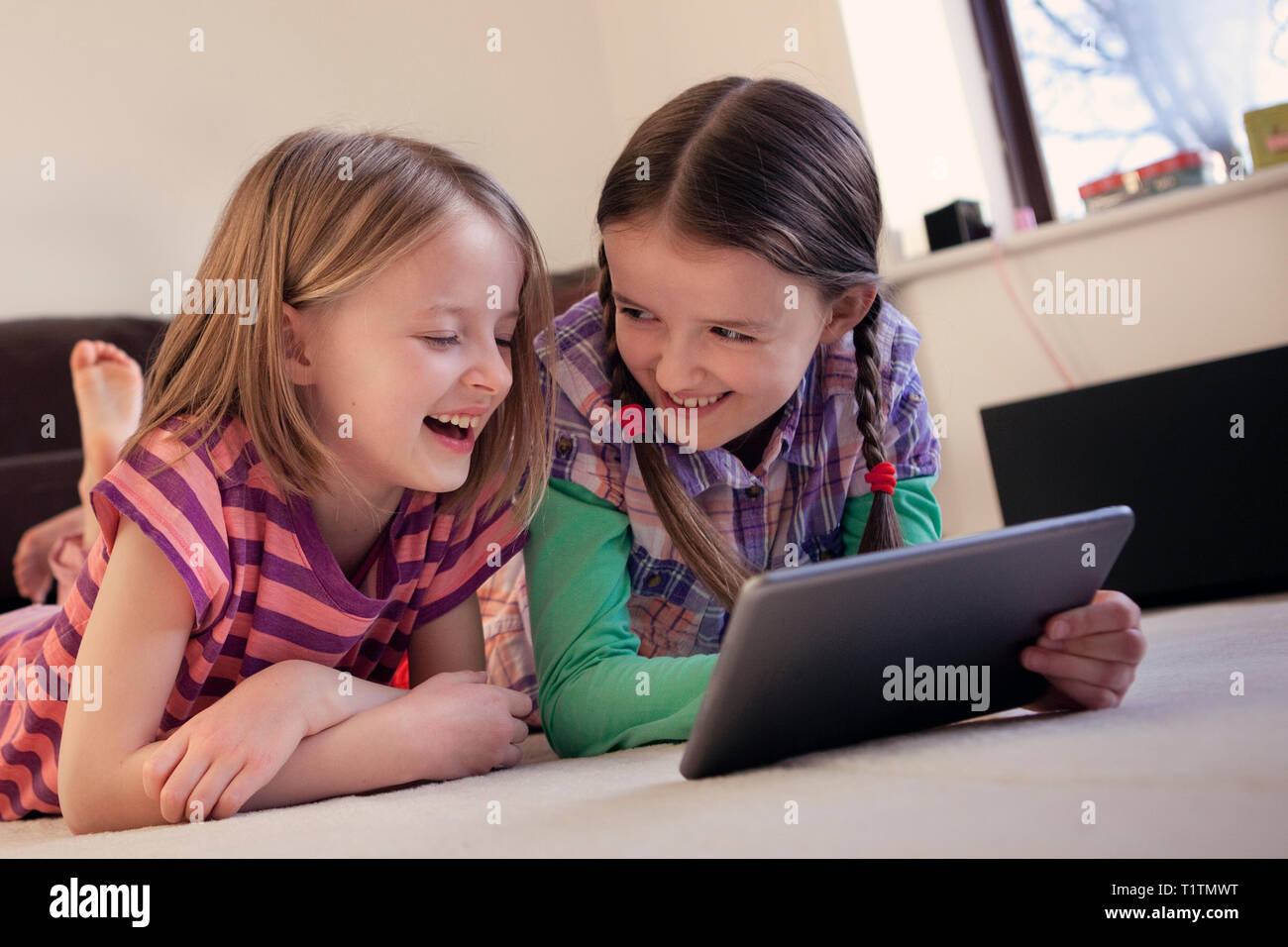Two happy, laughing children using a tablet device together Stock Photo