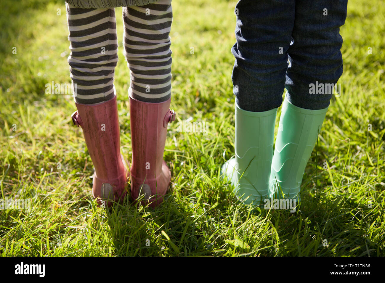 Low angle crop and rear view of two children wearing rubber boots and standing on summer grass Stock Photo