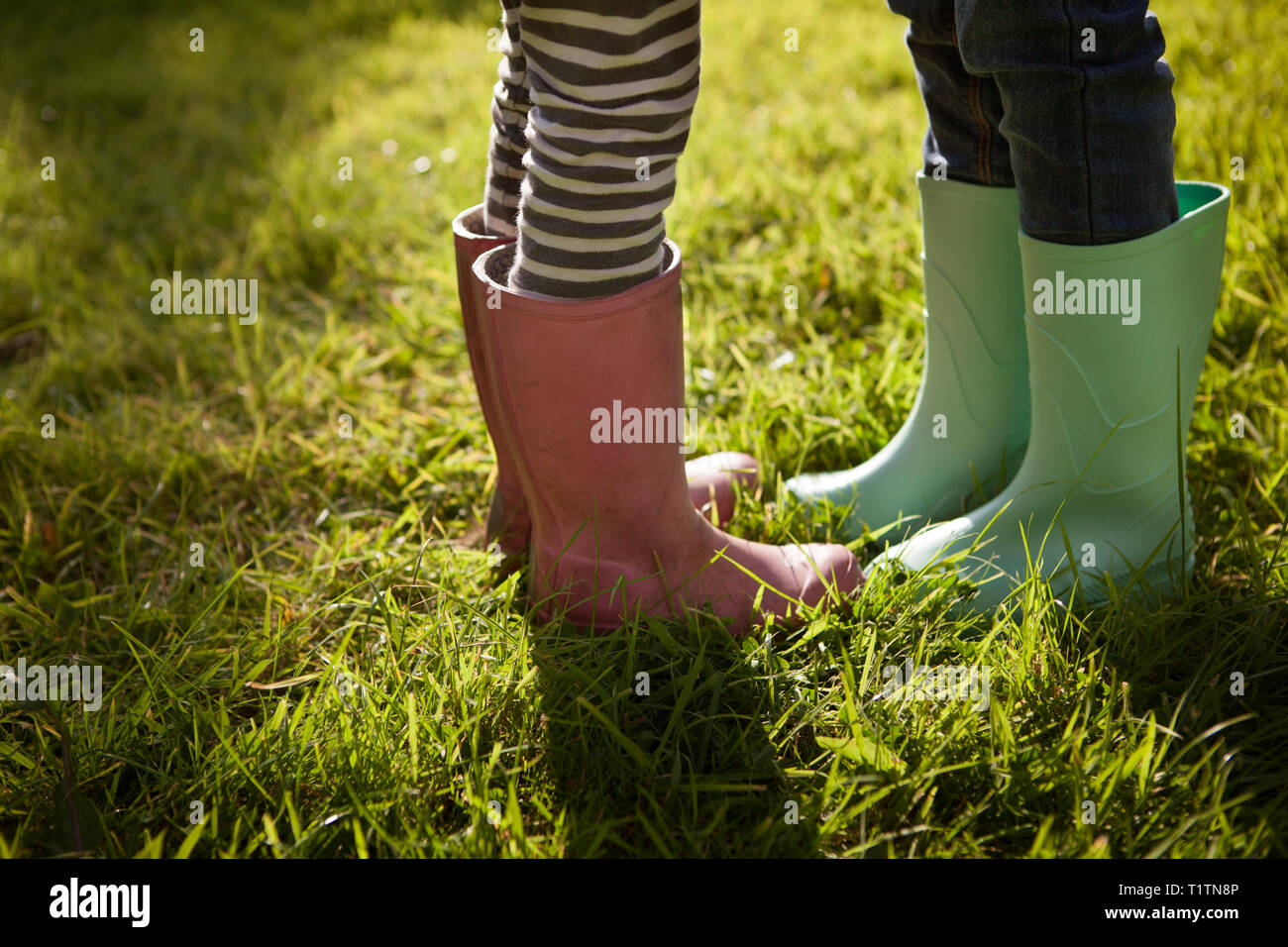 Low angle crop and side view of two children wearing rubber boots and standing on summer grass Stock Photo