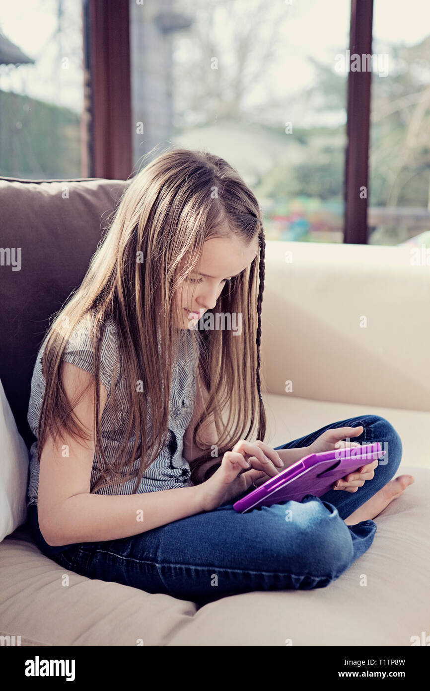 Girl sitting on a sofa and using a digital tablet device Stock Photo