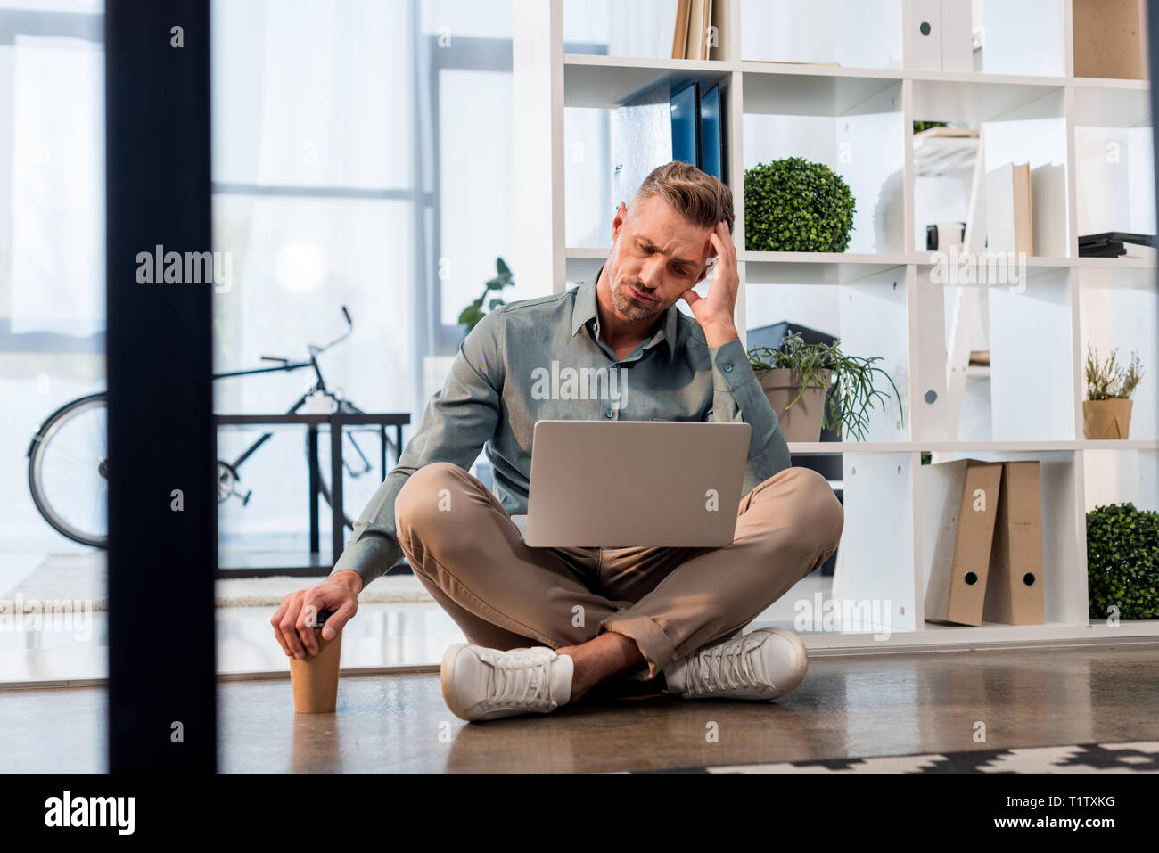 handsome businessman sitting with crossed legs on floor and looking at ...