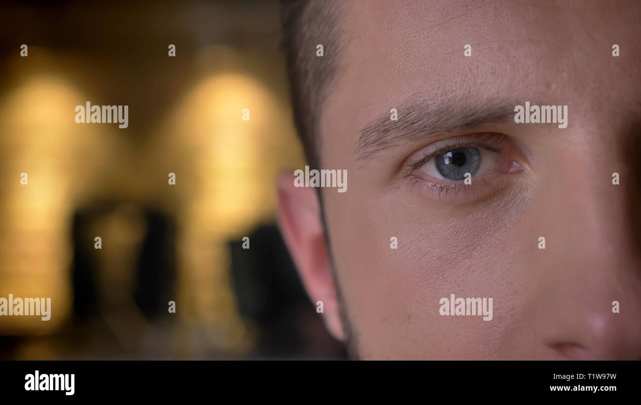 Closeup half-face front shoot of adult caucasian male eye looking at camera indoors with interior on the background Stock Photo