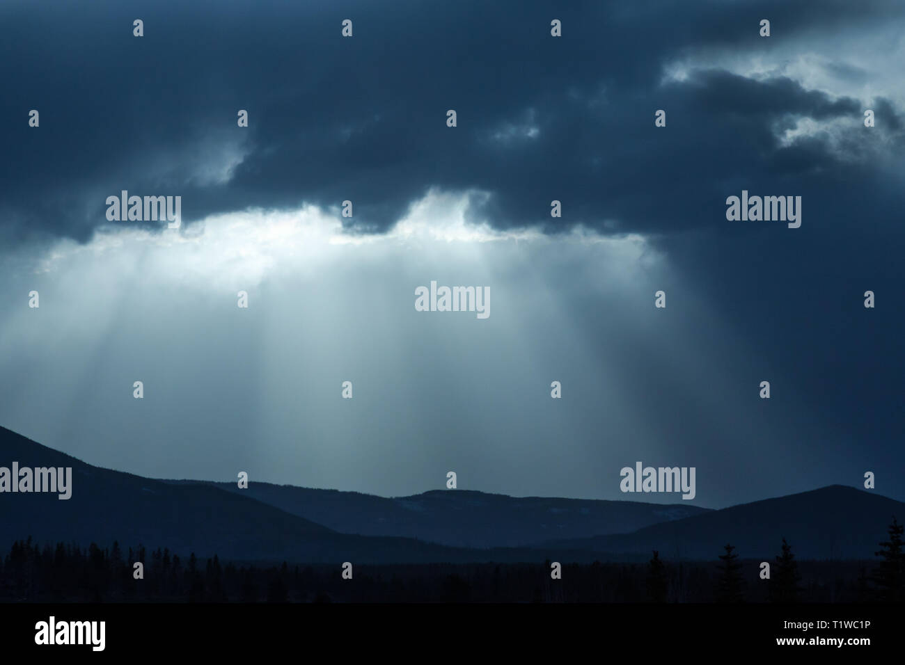 Beautiful image of blue sky with 'God rays' coming down to mountains with darker clouds above. Stock Photo