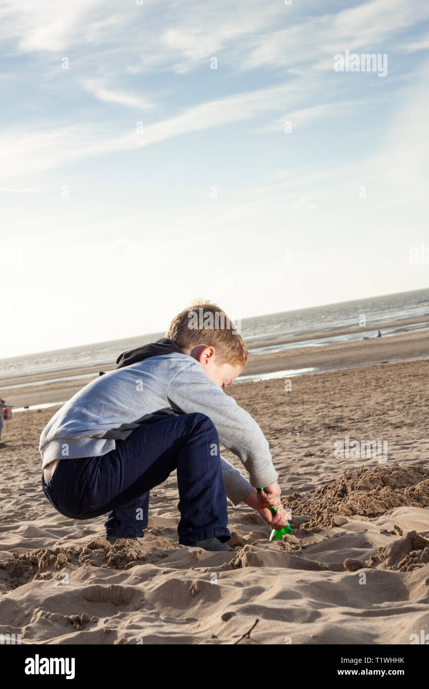 A young caucasian boy digging a hole in the sand at Formby beach, Merseyside, UK. Stock Photo