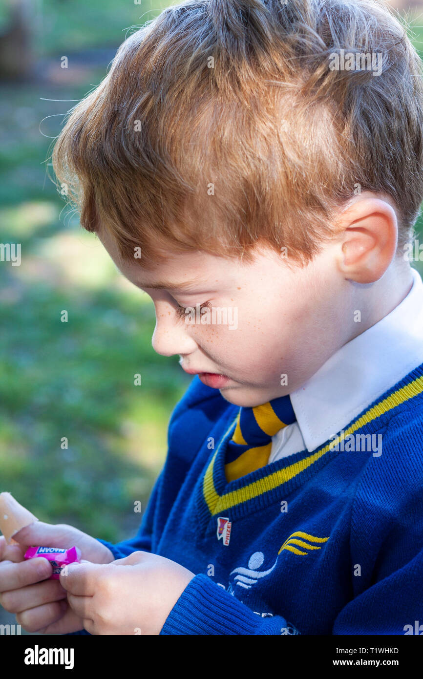A young schoolboy unwrapping a sweet Stock Photo