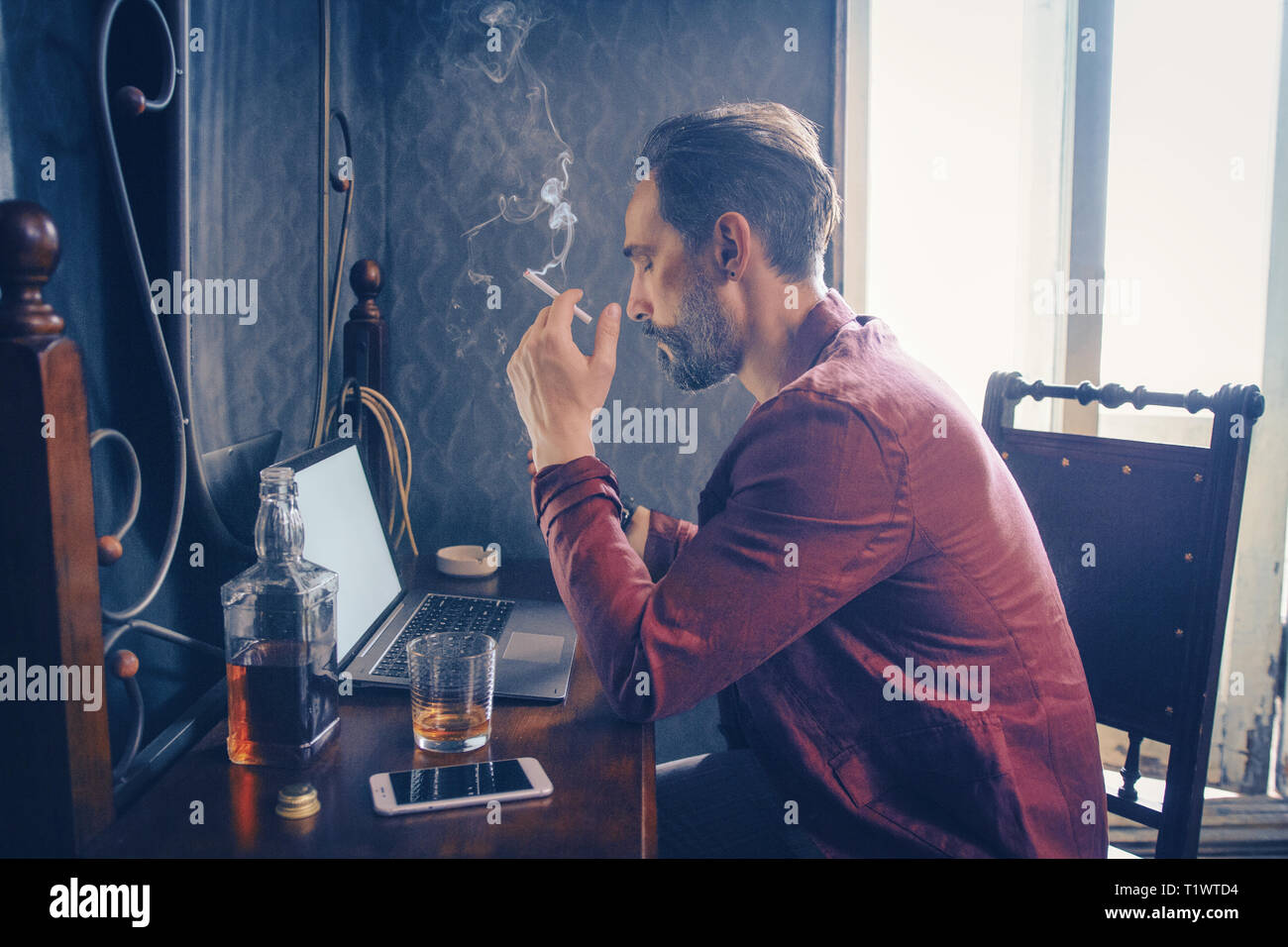 Handsome man works on his laptop smoking and drinking Stock Photo