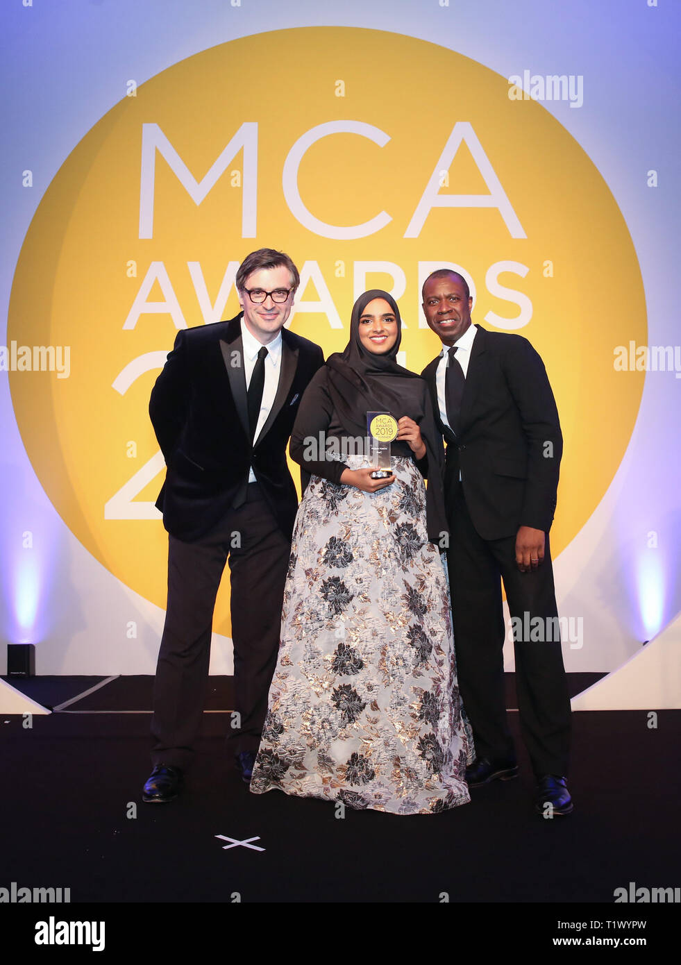 EDITORIAL USE ONLY (left to right) John Crowley (Digital Editor at The Times, Anjum Hakim PwC and Newsreader Clive Myrie after was awarded The Times Consultant of the Year at the 2019 MCA Awards at the Park Plaza Westminster in London, for her work on sensitive projects including rehousing victims of a disaster and driving digital change with a defence and security client. Stock Photo