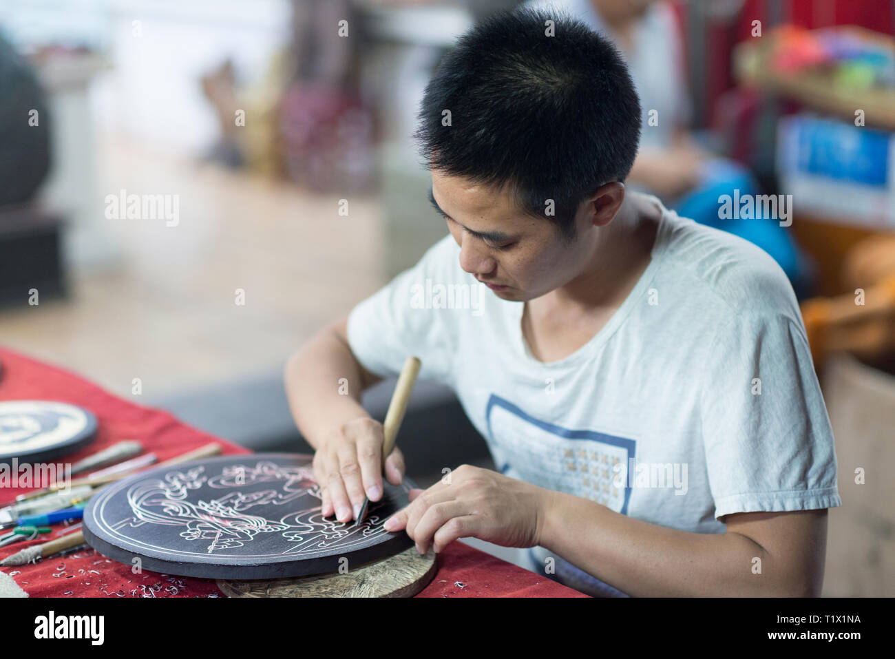 Dunhuang, China - 08 06 2016: A craftsman depicts Dunhuang culture through wood carvings. A chinese artist carving figures into a round of wood Stock Photo
