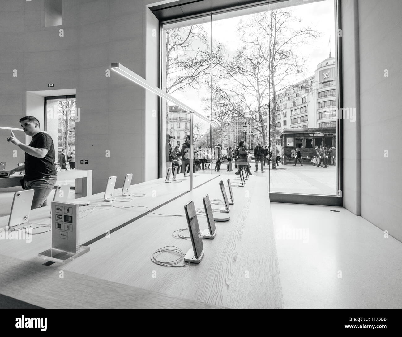 Paris, France - Mar 19 2019: Apple iPhone XS smartphones products are displayed inside the new Apple Store Champs-Elysees with people admiring burnt kiosk outside after yellow vests protest Stock Photo