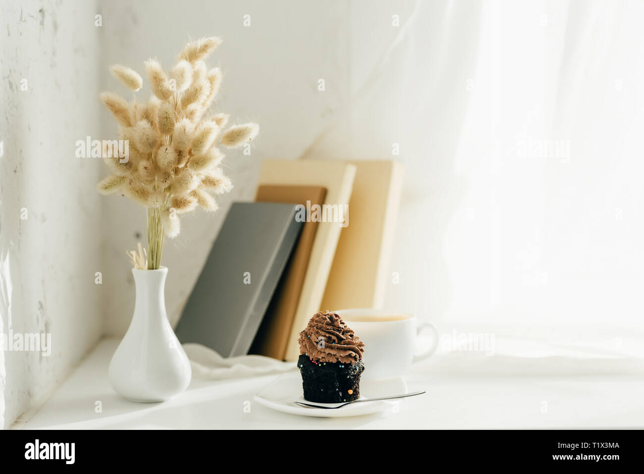 willow catkins in vase near cupcake, cup of coffee and books Stock Photo