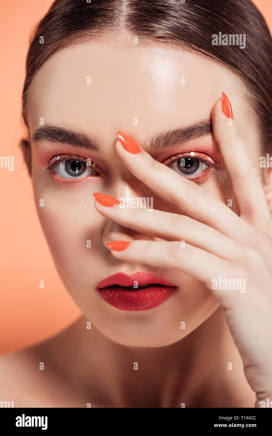 beautiful stylish young woman covering face with hand and posing isolated on coral Stock Photo