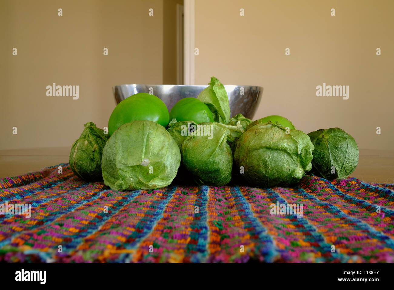 A pile of green tomatillos (Physalis philadelphica) on a colorfully patterned fabric; tomatillos with husks; peeled tomatillos. Stock Photo