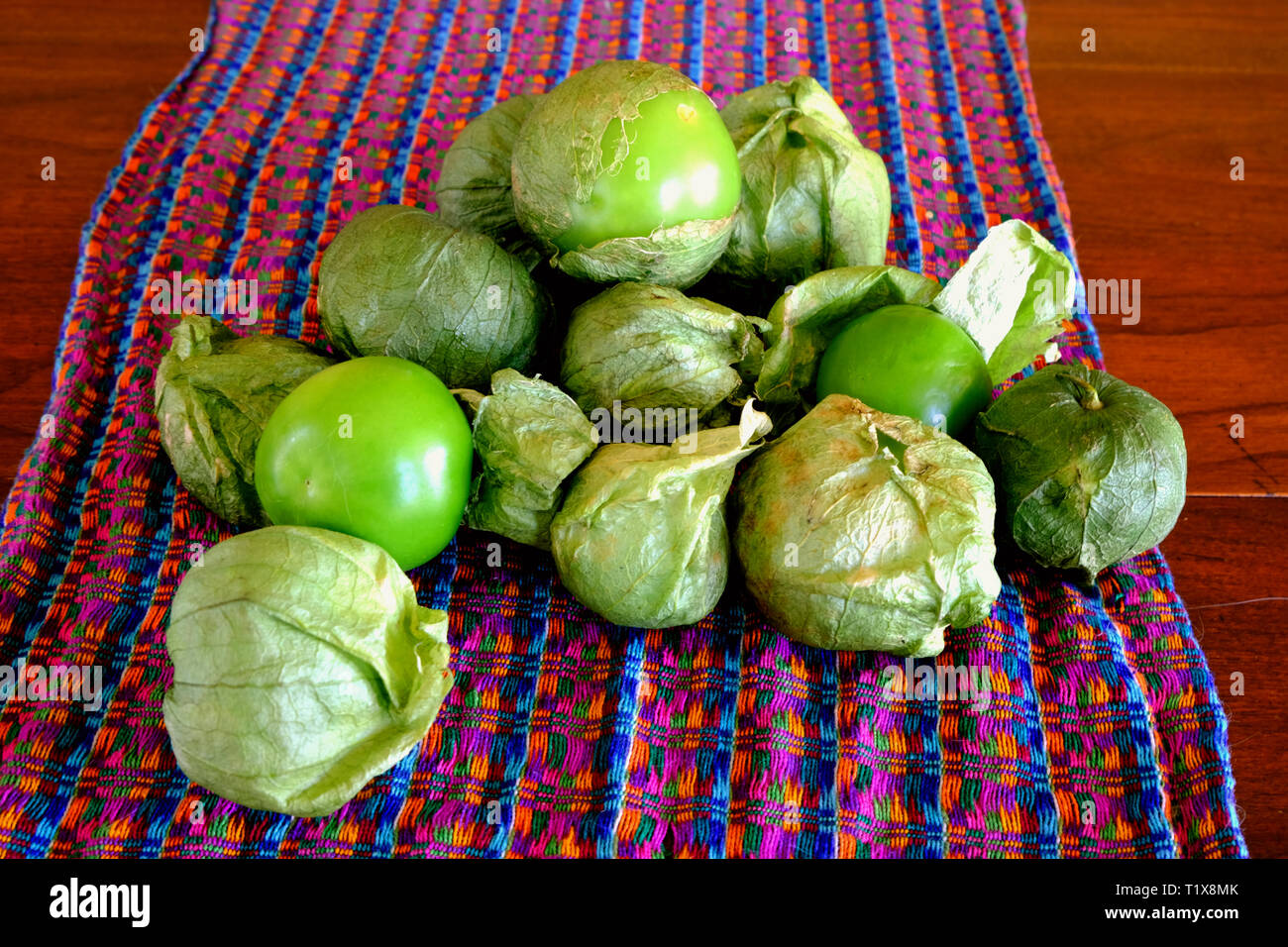 A pile of green tomatillos (Physalis philadelphica) on a colorfully patterned fabric; tomatillos with husks; peeled tomatillos. Stock Photo