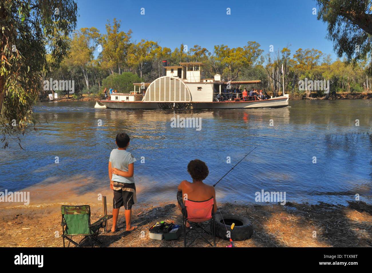 Restored paddle steamer 'Adelaide' on the Adelaide River in South Australia. Two kids fishing watch from shore, Eucalyptus trees at rivers edge. Stock Photo