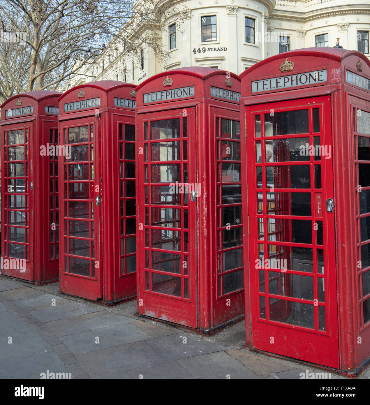 Four red traditional and heritage telephone boxes or kiosks stand in a row on the Strand, London, England, UK opposite Charing Cross Station. Stock Photo