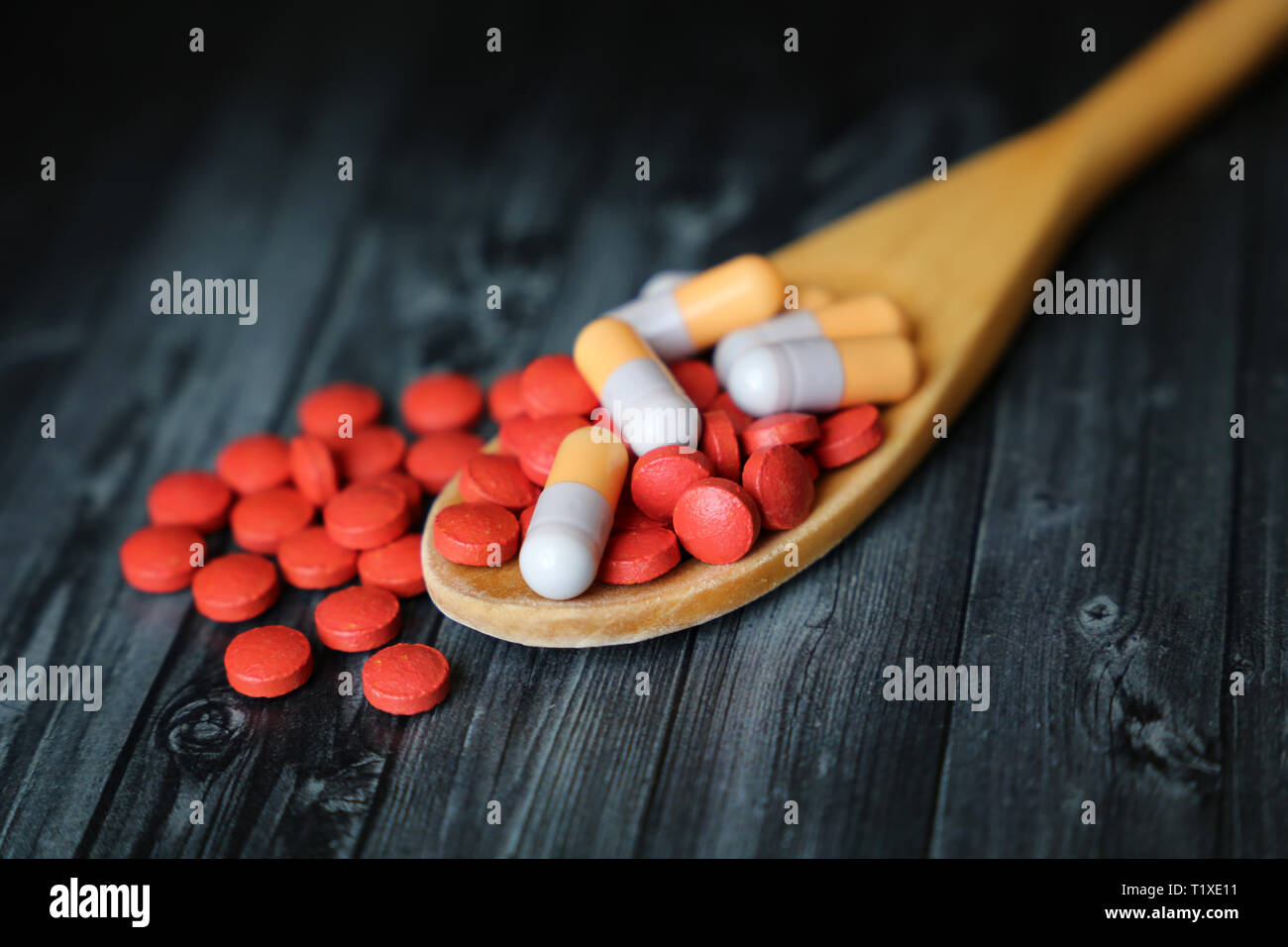 Pills and capsules in wooden spoon on dark vintage table. Concept of drugs, vitamins, pharmacy, cold and flu treatment Stock Photo