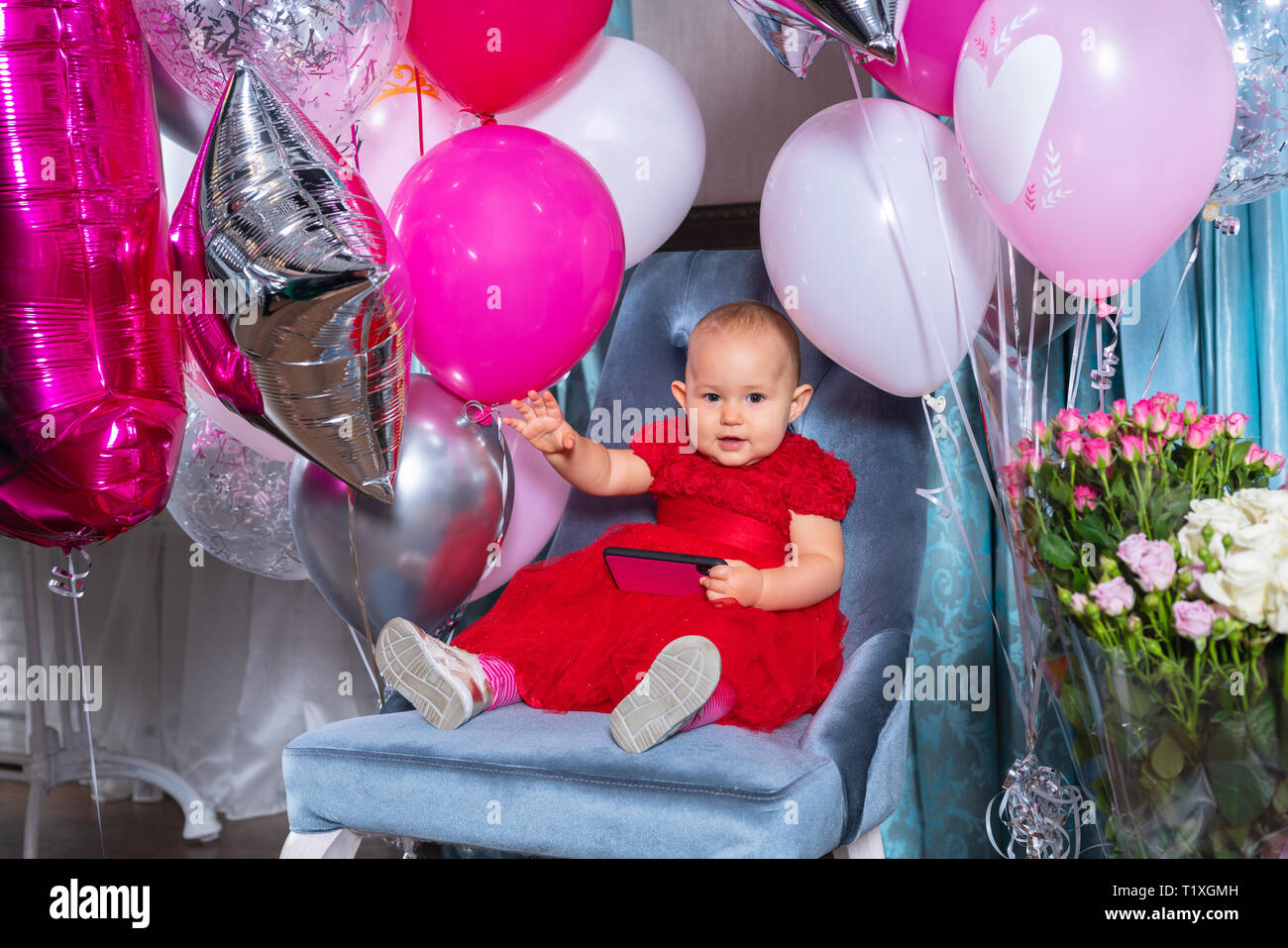 Happy little girl waving at the camera while celebrating her first birthday seated in a chair