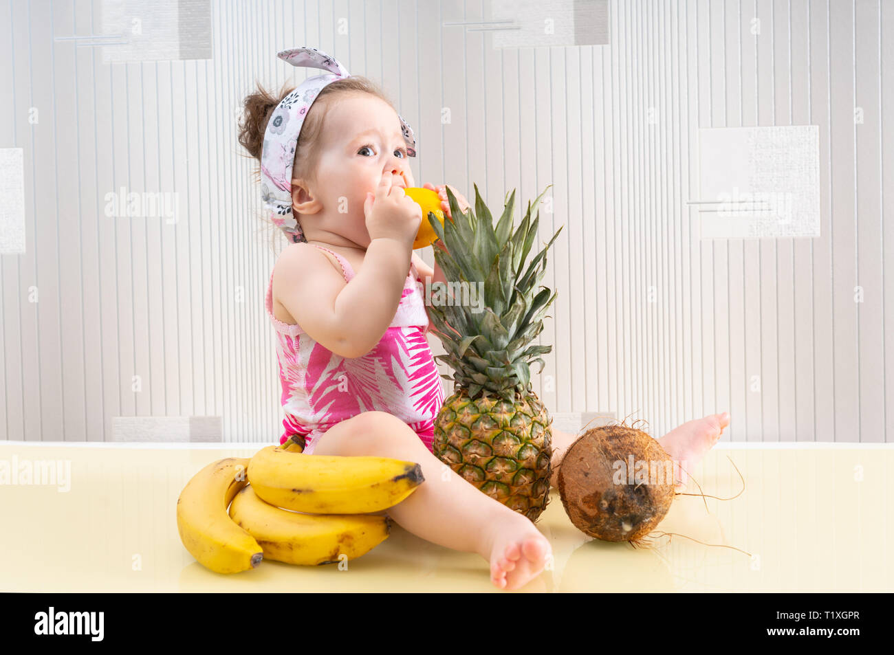 https://c8.alamy.com/comp/T1XGPR/cute-little-baby-girl-in-pink-shirt-sitting-among-tropical-fruits-on-table-surface-and-eating-a-sour-lemon-viewed-from-the-side-T1XGPR.jpg