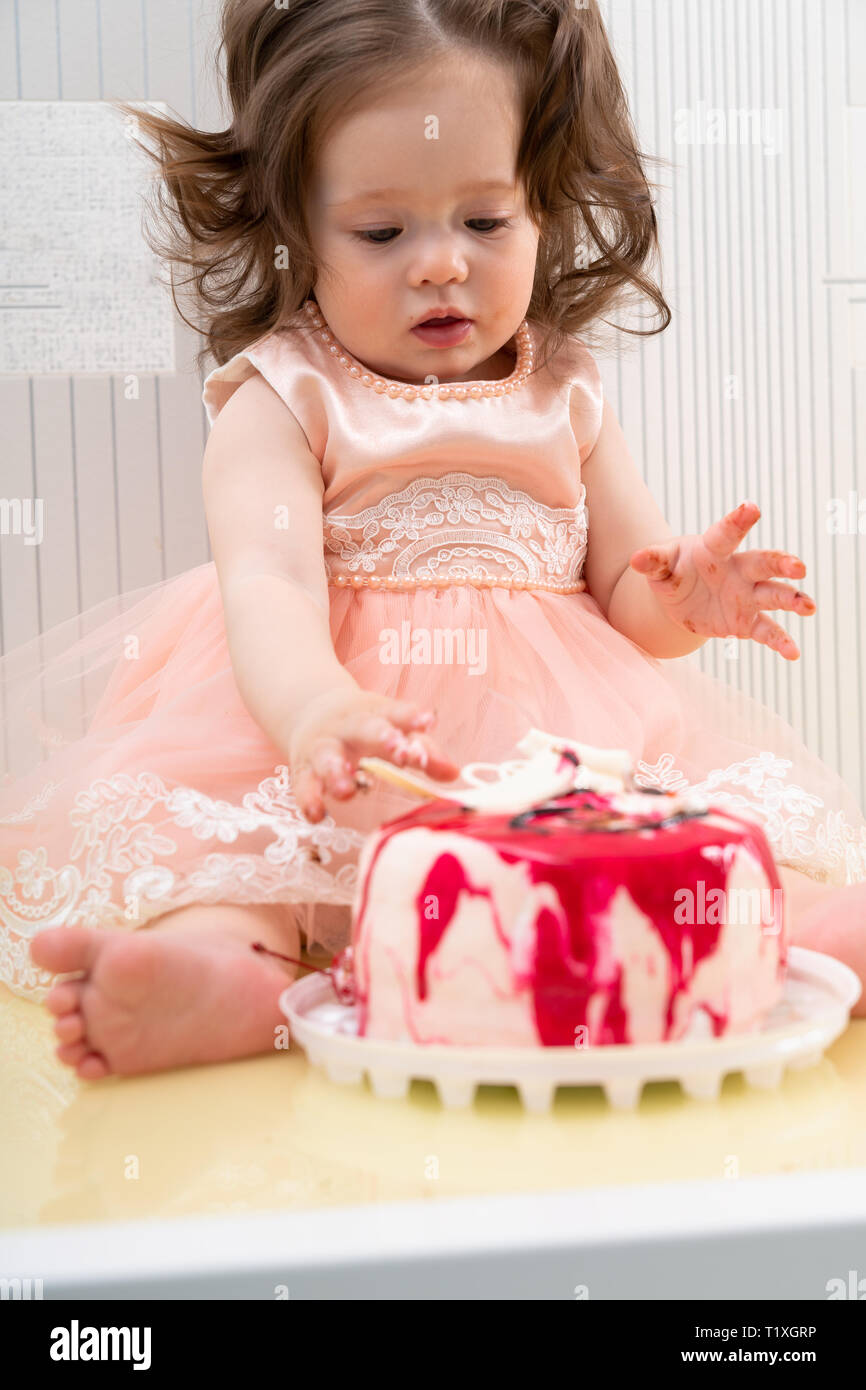 Cute little girl in holiday pink dress sitting on table surface and ...