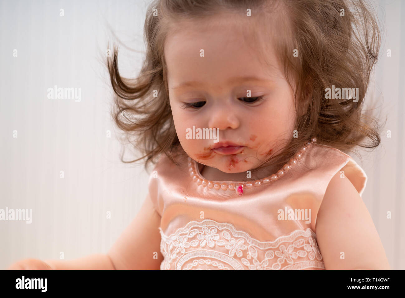 Cute little girl with a dirty sticky face full of red jelly from eating her birthday cake in a close up cropped portrait Stock Photo