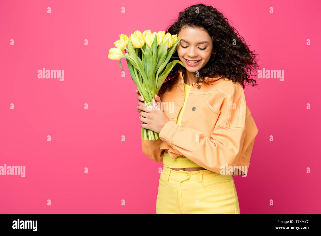 attractive smiling african american girl holding yellow tulips isolated on crimson Stock Photo