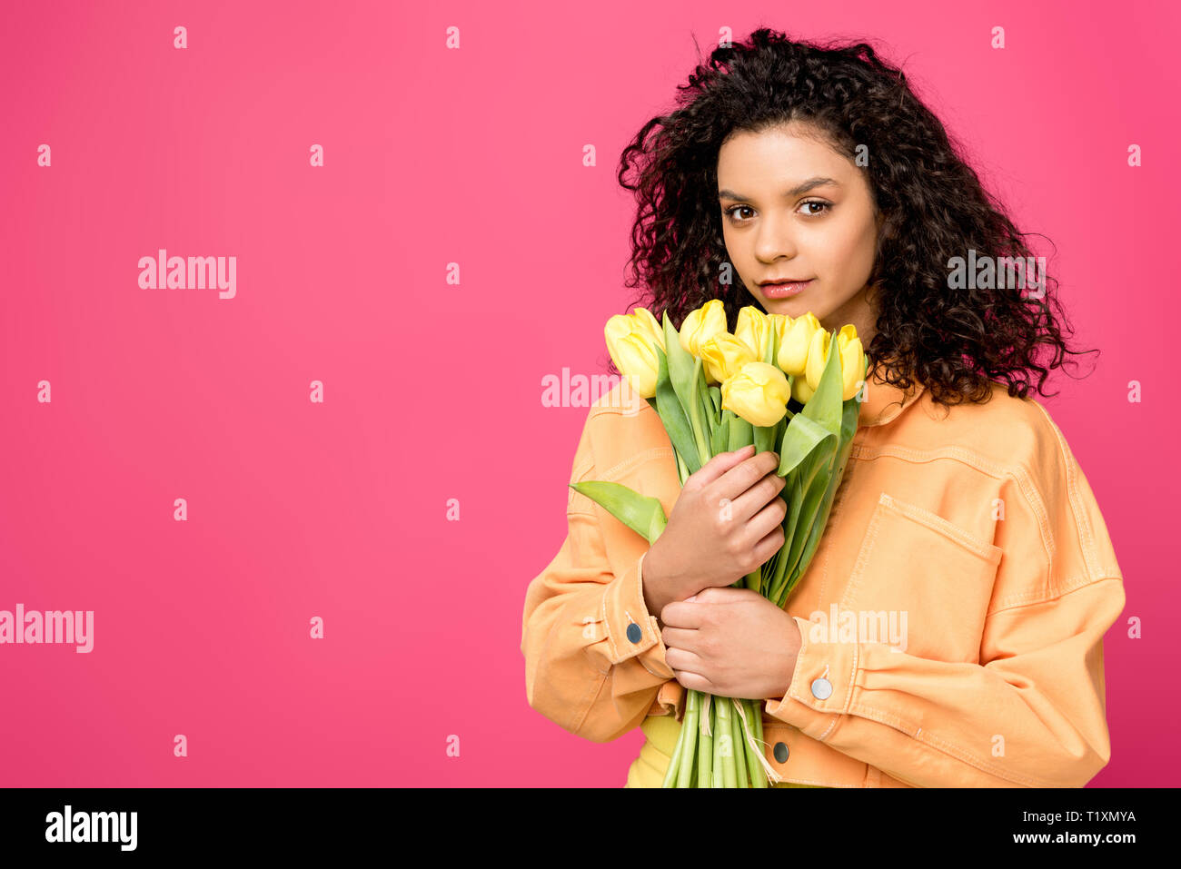 attractive curly african american girl holding yellow tulips isolated on crimson Stock Photo