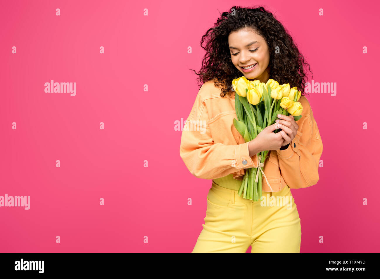 smiling african american girl holding yellow tulips isolated on crimson Stock Photo