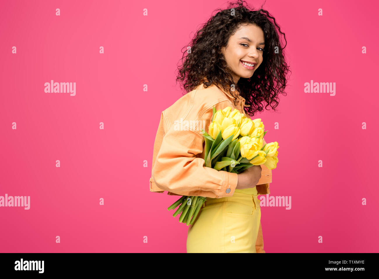 smiling african american woman holding yellow tulips isolated on crimson Stock Photo